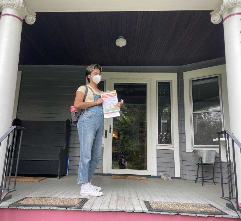 MNYC door knocking - student standing on porch holding clipboard
